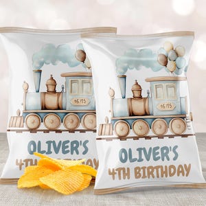 May include: Two white chip bags with a watercolor train design, balloons, and the text "Oliver's 4th Birthday." The train is light blue and brown. A small pile of chips is in front of the bags.