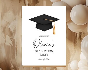 Può includere: Un cartello rettangolare bianco per una festa di laurea con un tocco nero e una nappa dorata. Il testo recita: WELCOME TO Olivia's GRADUATION PARTY class of 20xx. Il cartello è esposto su un cavalletto in legno.