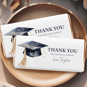 May include: Two white chocolate bar wrappers with a blue graduation cap and gold tassel design. The text on the wrappers reads "Thank you for your love & support" and "love, Taylor".
