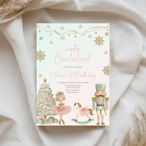 May include: A rectangular birthday invitation card featuring a light blue and pink gradient background with gold snowflakes and ribbons. It displays the text Winter Onederland, Olivia's 1st Birthday, and event details alongside a Christmas tree, a ballerina, a rocking horse, and a nutcracker.