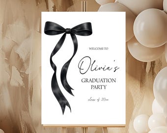 Può includere: Un cartello bianco per una festa di laurea su un cavalletto, con un'illustrazione di un fiocco nero. Il cartello recita "Benvenuti alla festa di laurea di Olivia" con l'anno della classe sottostante. Palloncini sullo sfondo.