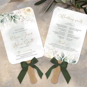 Puede incluir: Dos abanicos de boda blancos con diseños florales verdes y dorados. Los abanicos tienen mangos de madera con cintas de satén verde. El texto en los abanicos dice "Bienvenido a la boda de Oline Jones y Aaron Smith" y "Wedding Party".