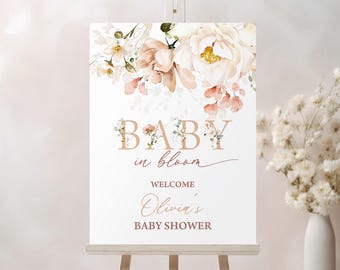 May include: A white welcome sign with a floral design in shades of pink and white. The text reads "Baby in bloom" and "Welcome Olivia's Baby Shower".