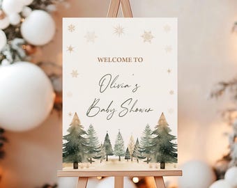 May include: A rectangular sign on a wooden easel, featuring the text "WELCOME TO Olivia's Baby Shower" in elegant script. The sign has a winter theme with snowflakes and watercolor pine trees at the bottom. The background is a soft cream color.