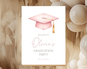 Può includere: Un cartello di benvenuto per una festa di laurea su un cavalletto. Il cartello presenta un'illustrazione di cappello di laurea rosa e il testo "Welcome to Olivia's Graduation Party". Palloncini bianchi e beige sullo sfondo.
