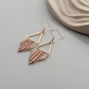 Könnte beinhalten: Goldene Dreiecksohrringe mit einer Perlenfransen in Weiß- und Roségoldtönen.