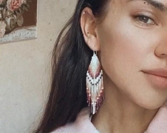 May include: A woman wearing a pink fleece jacket with a zipper. She is wearing long, beaded earrings with a pink, white, and black color scheme.