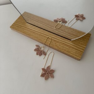 May include: A pair of delicate gold earrings with pink flower-shaped charms. The earrings are hanging from a wooden surface.