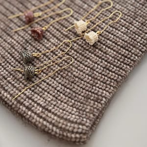 May include: A set of six gold dangle earrings with different colored beaded charms. The earrings are displayed on a brown knitted surface.