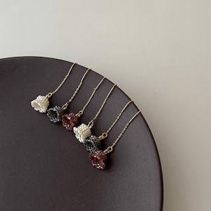 May include: Four pairs of delicate gold chain earrings with small, beaded, bell-shaped charms in white, burgundy, and gray.