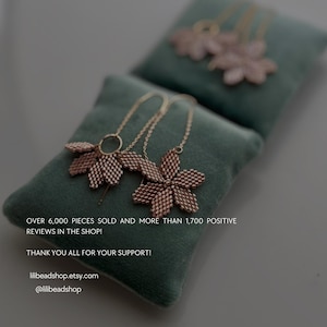 May include: Two delicate gold necklaces with rose gold flower pendants on a green velvet surface. The text "OVER 6,000 PIECES SOLD AND MORE THAN 1,700 POSITIVE REVIEWS IN THE SHOP! THANK YOU ALL FOR YOUR SUPPORT! lilibeadshop.etsy.com @lilibeadshop" is printed below the necklaces.