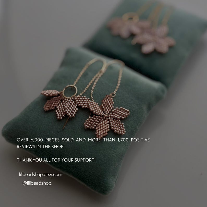 May include: Two delicate gold necklaces with rose gold flower pendants on a green velvet surface. The text "OVER 6,000 PIECES SOLD AND MORE THAN 1,700 POSITIVE REVIEWS IN THE SHOP! THANK YOU ALL FOR YOUR SUPPORT! lilibeadshop.etsy.com @lilibeadshop" is printed below the necklaces.