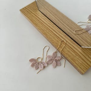 May include: A pair of delicate pink flower-shaped earrings with gold chain and hoop accents.