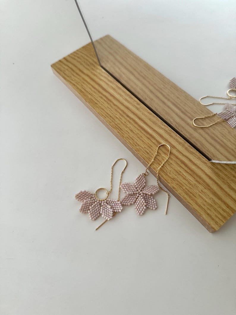 May include: A pair of delicate pink flower-shaped earrings with gold chain and hoop accents.
