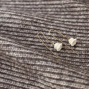 May include: A pair of delicate gold earrings with small white bell charms hanging from thin chains.