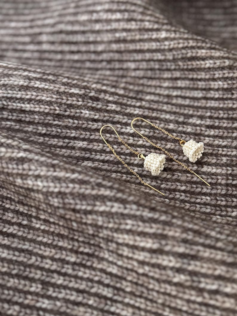 May include: A pair of delicate gold earrings with small white bell charms hanging from thin chains.