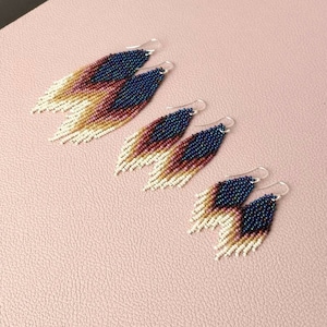May include: Three pairs of beaded earrings in graduated sizes. The earrings are made with small, colourful beads in shades of white, beige, pink, red, and blue. The earrings have a teardrop shape and dangle from silver hooks.