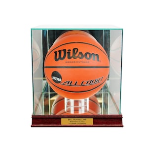 May include: An orange Wilson basketball in a clear display case. The ball has black text that reads "Wilson Indoor/Outdoor" and "NCAA All Court". A gold plaque at the base reads "Bill Russell #6 Boston Celtics 11x NBA Champion".