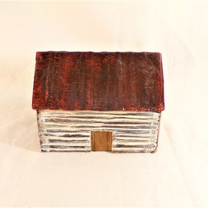 May include: A small, whitewashed log cabin with a red roof. The cabin has a single door and is made of wood.