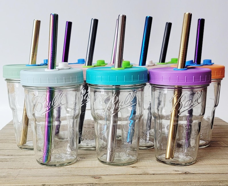 May include: Clear glass Ball mason jars with colorful lids and metal straws. The lids are in various colors, including blue, green, purple, and orange. The straws have different metallic finishes.