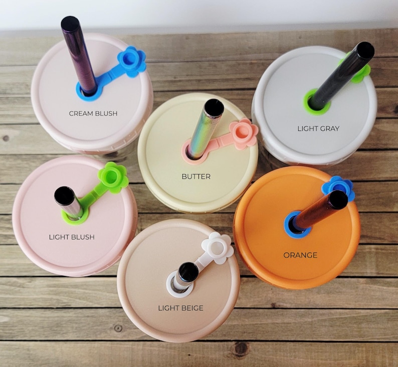 May include: Six mason jar lids in various colors, each with a straw and a flower-shaped holder. Colors include cream blush, light gray, light blush, butter, light beige, and orange. Each lid has a different colored straw and holder, with the color names printed on the lid.
