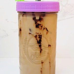 K&ouml;nnte beinhalten: Ein klares Glasgef&auml;&szlig; gef&uuml;llt mit beiger Fl&uuml;ssigkeit und dunkelbraunen Wirbeln, mit violettem Deckel, Metallstrohhalm und gr&uuml;nem Verschluss. Text: THE PERFECT JAR, LEAKPROOF!!, THICK, HIGH QUALITY GLASS, 710 ML, 18 CM H&Ouml;HE, 8 CM DURCHMESSER.