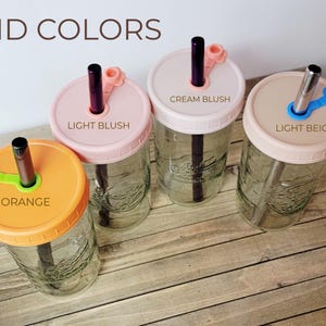 K&ouml;nnte beinhalten: Vier durchsichtige Einmachgl&auml;ser aus Glas mit Deckeln und Strohhalmen. Die Deckel sind mit Orange, Light Blush, Cream Blush und Light Beige beschriftet. Jeder Deckel hat einen passenden Silikonstopfen f&uuml;r den Strohhalm. Metallische Strohhalme.
