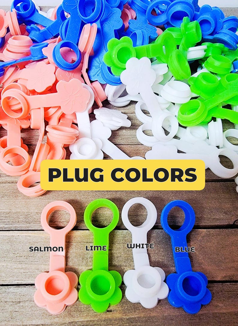 K&ouml;nnte beinhalten: Eine Sammlung von Silikonstopfen in den Farben Lachs, Limette, Wei&szlig; und Blau. Jeder Stopfen besteht aus einem kreisf&ouml;rmigen Ring, der an einer blumenf&ouml;rmigen Kappe befestigt ist. Der Text PLUG COLORS steht &uuml;ber vier einzelnen, beschrifteten Stopfen.