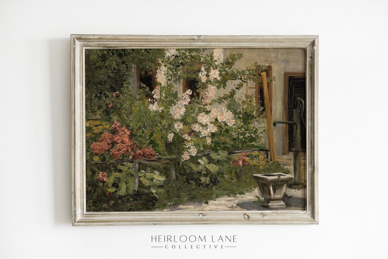 May include: A framed oil painting depicting a garden scene with a white building in the background. The garden is filled with lush greenery, pink flowers, and a stone well. The painting is framed in a light gray frame.