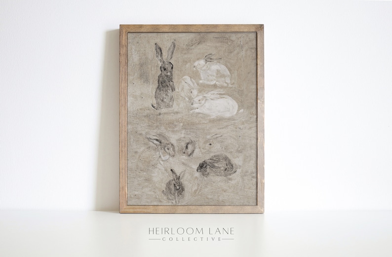 May include: A framed print of a vintage illustration featuring a group of rabbits in various poses. The rabbits are drawn in shades of gray and white on a beige background. The frame is a simple wooden frame with a light brown finish.
