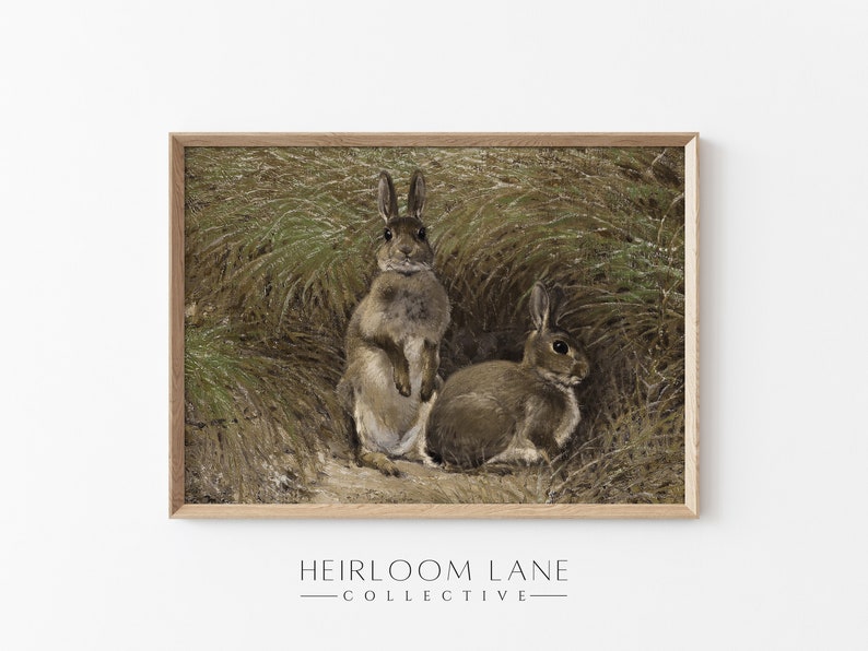 K&ouml;nnte beinhalten: Ein gerahmter Druck eines Gem&auml;ldes, das zwei braune Kaninchen in einem Feld mit hohem Gras zeigt. Das Kaninchen links steht aufrecht, w&auml;hrend das Kaninchen rechts liegt. Der Druck hat einen hellbraunen Holzrahmen.