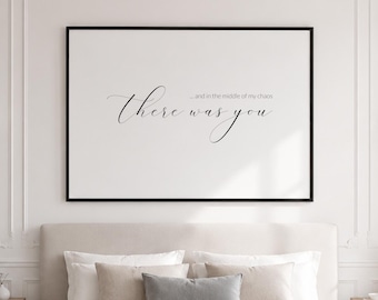 Puede incluir: Una impresión enmarcada con el texto "...and in the middle of my chaos there was you" en escritura elegante. El arte enmarcado en negro cuelga sobre una cama con ropa de cama y almohadas de tonos neutros. La habitación tiene una lámpara de araña y apliques.