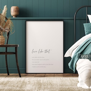 May include: A framed print with the words "love like that" in elegant script. Below, a poem about love is printed in a simple font. The print is displayed in a bedroom with teal walls and a neutral rug.