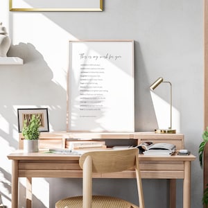 May include: A framed print with a white background and black text that reads "This is my wish for you" followed by a list of words including "comfort", "smiles", "rainbows", "laughter", "sunsets", "hugs", "beauty", "faith", "confidence", "courage", "patience", "love". The print is on a wooden desk with a potted plant, a lamp, and a chair.