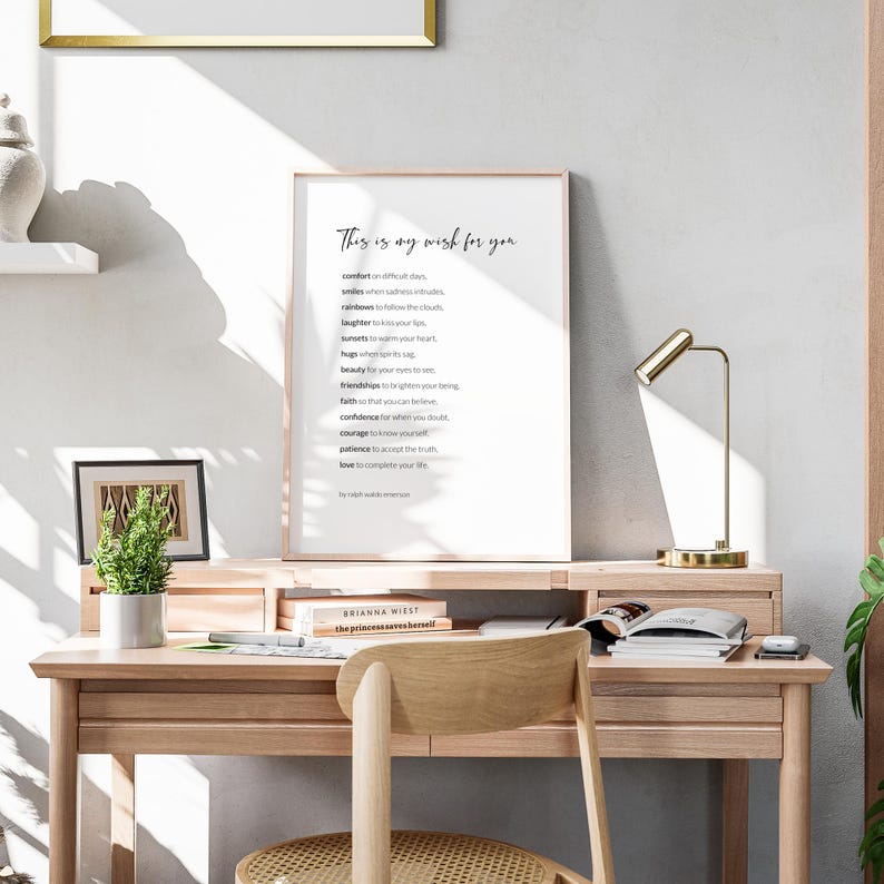 May include: A framed print with a white background and black text that reads "This is my wish for you" followed by a list of words including "comfort", "smiles", "rainbows", "laughter", "sunsets", "hugs", "beauty", "faith", "confidence", "courage", "patience", "love". The print is on a wooden desk with a potted plant, a lamp, and a chair.
