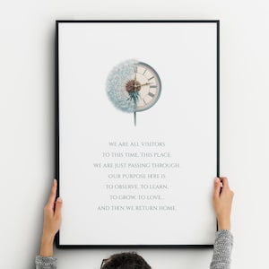 May include: A framed print with a dandelion clock design. The clock face is combined with a dandelion, and the print includes the text: "WE ARE ALL VISITORS TO THIS TIME, THIS PLACE..." The print is held by a person.