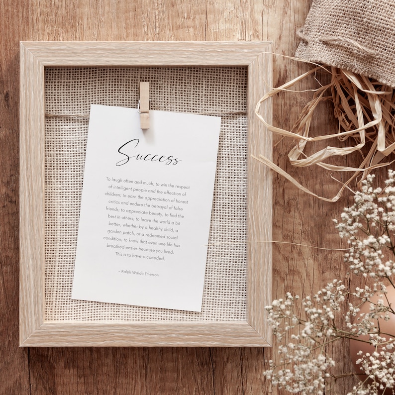 Puede incluir: Una impresi&oacute;n enmarcada con la palabra "Success" en escritura elegante. La impresi&oacute;n se sujeta con una pinza de madera dentro de un marco de madera de color claro. El texto incluye una cita de Ralph Waldo Emerson. El fondo es una superficie de madera con elementos decorativos.