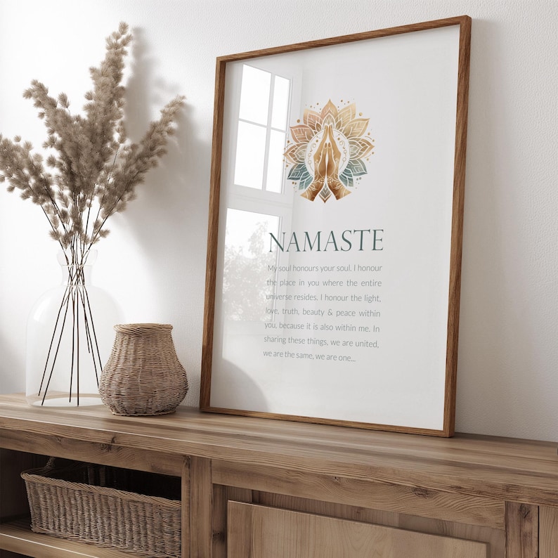May include: A framed print featuring a watercolour illustration of hands in a prayer position with a mandala design. The text "NAMASTE" is written in a blue font with a definition below in a smaller font.