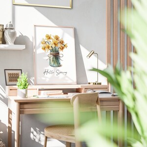 以下が含まれることがあります： 白い背景に、「Hello Spring」というテキストが書かれたガラス瓶に入った黄色の水仙の花束の水彩画プリントです。