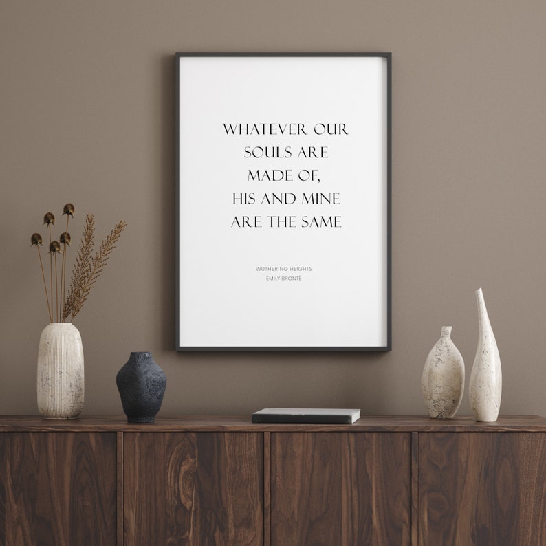 Puede incluir: Una impresi&oacute;n enmarcada en negro con fondo blanco y el texto "WHATEVER OUR SOULS ARE MADE OF, HIS AND MINE ARE THE SAME" con el t&iacute;tulo "WUTHERING HEIGHTS" y el autor "EMILY BRONTE" debajo. La impresi&oacute;n se muestra en un estante de madera con dos jarrones de cer&aacute;mica blanca y un jarr&oacute;n de cer&aacute;mica azul oscuro.
