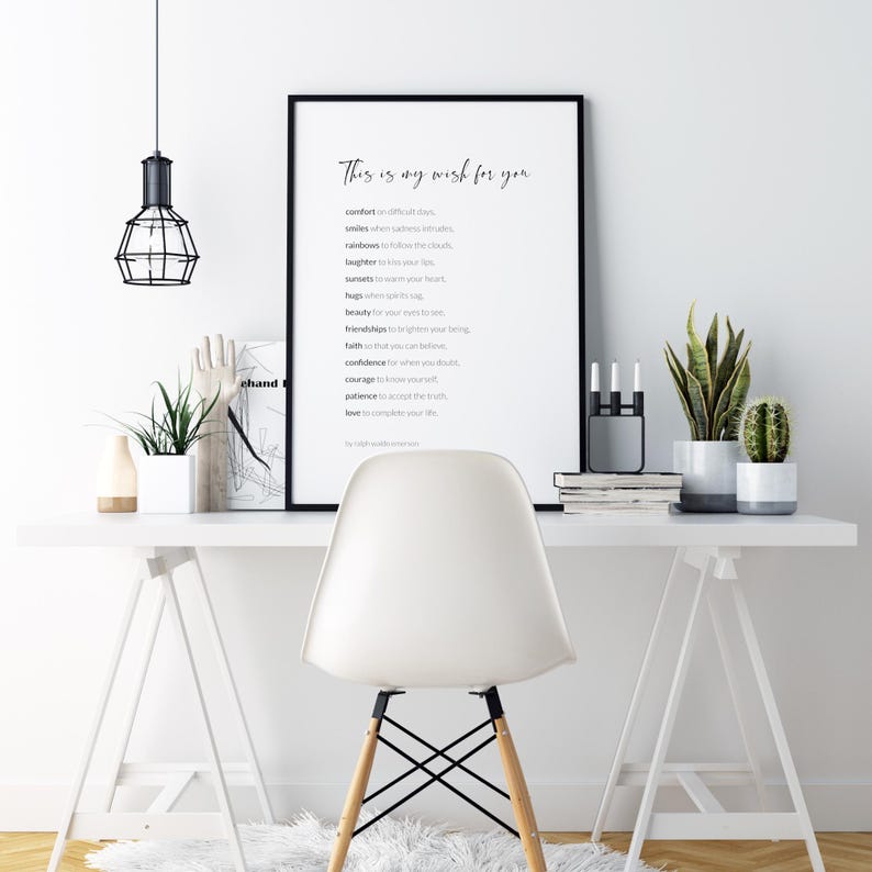 May include: A black framed print with a white background and black text that reads "This is my wish for you" followed by a list of words including comfort, smiles, rainbows, laughter, summers, beauty, hugs, friendships, faith, confidence, courage, patience, and love. The print is hanging on a white wall above a white desk with a white chair, a potted plant, and a black candle holder.