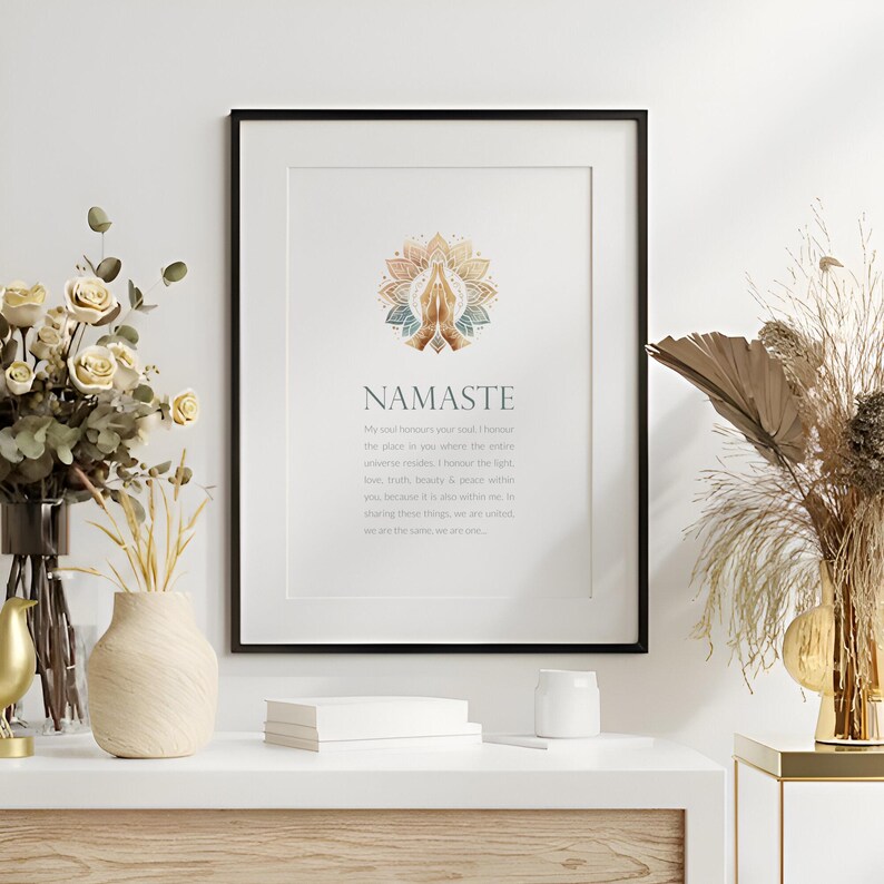 May include: A framed print with a white background and black frame. The print features a gold and blue mandala with a pair of hands in a prayer position. The text "Namaste" is written in a gold font below the mandala. The text below "Namaste" reads "My soul honours your soul, I honour the place in you where the entire universe resides. I honour the light, love, truth, beauty & peace within you, because it is also within me. Sharing these things, we are united, we are the same, we are one."