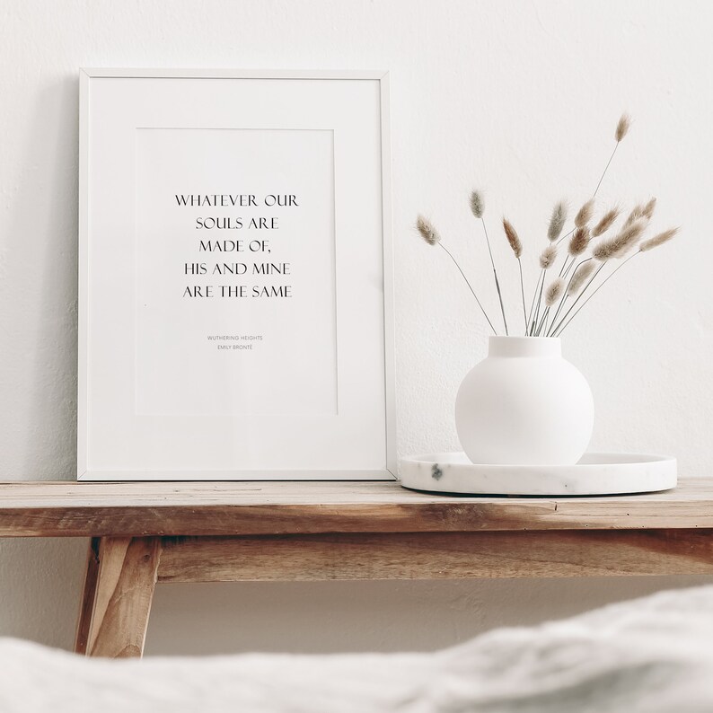 Puede incluir: Una impresi&oacute;n enmarcada en blanco con la cita "Whatever our souls are made of, his and mine are the same" de Cumbres Borrascosas de Emily Bront&euml;. La impresi&oacute;n est&aacute; sobre una mesa de madera con un jarr&oacute;n blanco de hierba de la pampa seca.
