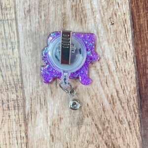 Op de afbeelding: Paarse glitter badge reel met een transparante plastic badgehouder en een zilveren clip. De reel heeft een transparante plastic bedel met een zilveren strass.