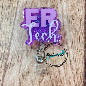 Op de afbeelding: Paarse glitter badgehouder met een wit "ER Tech" ontwerp. De badgehouder heeft een transparante plastic clip en een transparante plastic band.
