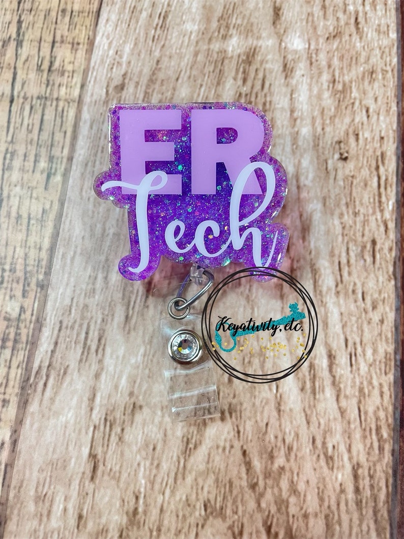 Op de afbeelding: Paarse glitter badgehouder met een wit "ER Tech" ontwerp. De badgehouder heeft een transparante plastic clip en een transparante plastic band.