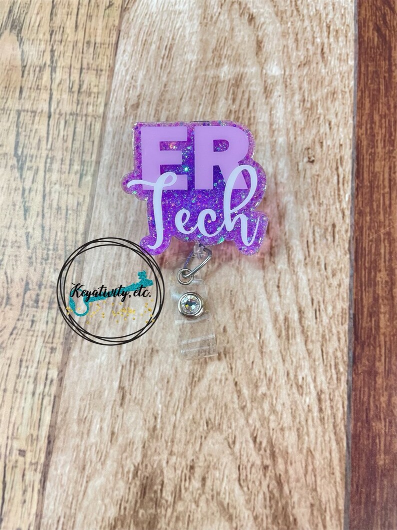 Op de afbeelding: Paarse glitterhars badgehouder met een wit "ER Tech" ontwerp. De badgehouder heeft een transparante, intrekbare plastic reel.