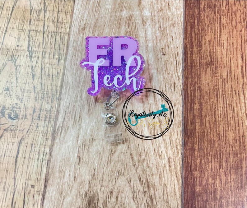 Op de afbeelding: Paarse glitter badge reel met een witte "ER Tech" inscriptie. De reel heeft een transparante plastic behuizing en een zilveren intrekbaar koord.