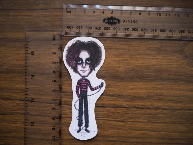 May include: A sticker featuring a cartoon illustration of a person with dark hair and a pink and black striped shirt holding a microphone. The person is wearing black pants and black shoes.