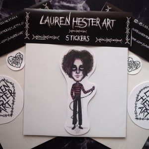 May include: A set of three stickers featuring a cartoon illustration of a person with black hair and a red and black striped shirt holding a microphone. The stickers are on a white background with black barbed wire around the edges. The text "LAUREN HESTER ART" is printed on the stickers.